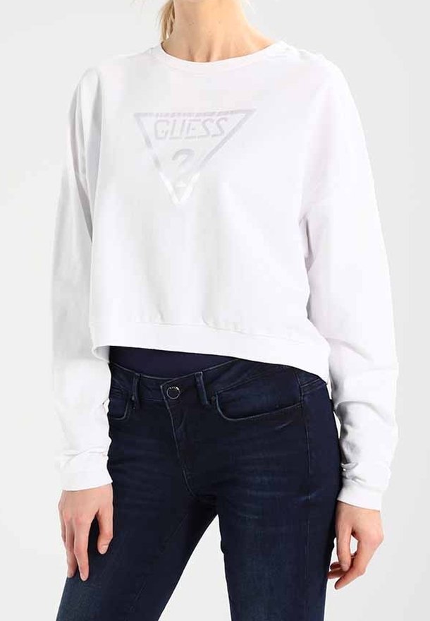 Sudadera recortada blanca con un diseño de logo triangular en el centro, combinada con jeans ajustados de color azul oscuro. Textura suave y mangas largas.