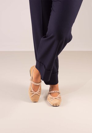 Bailarinas beige con detalle de lazo, acabado de ante, y correa decorativa con rhinestones, llevadas con pantalones navy ajustados.