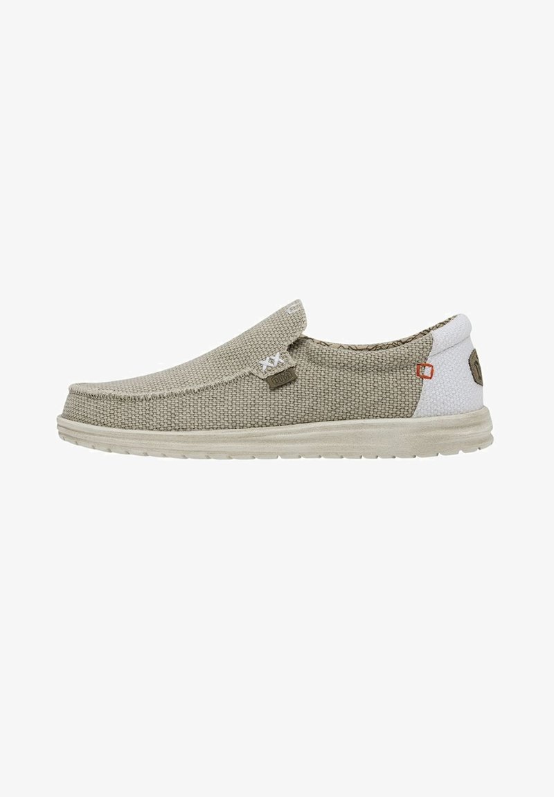 Zapatos slip-on beige con una parte superior de tejido texturizado, suela gris claro y sección de talón blanca a contraste. Presentan un branding mínimo y detalles de costura.