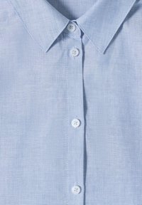 Chemise habillée bleu clair avec col pointu et quatre boutons blancs boutonnés au centre devant.