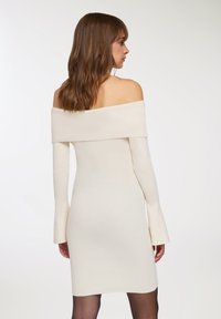 Abito con scollatura a spalla, in bianco crema con un design a coste. Maniche lunghe e aderenti e una silhouette dritta. Tessuto a maglia liscio senza chiusure visibili.