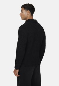 Maglione nero a trama con colletto, realizzato in un materiale morbido e lanoso; aderente, con maniche lunghe e orlo dritto.