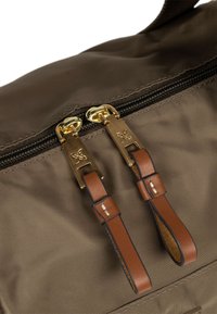 Sac en nylon marron avec deux zips dorés et des tirettes en cuir, présentant une texture lisse et un design épuré et minimaliste.