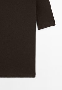 Tmavě hnědé tričko s krátkým rukávem a viditelným šitím na rukávech a spodním lemu, zobrazené na bílém pozadí.