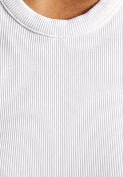 White ribbed fabric with a round neckline. Close-up view highlights the texture and fine vertical patterns creating a subtle surface detail.