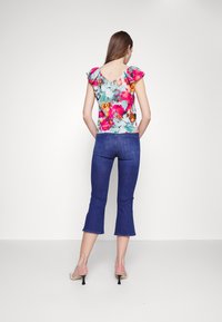 Top de estampado floral con mangas cortas con volantes, combinado con jeans azules cortos. Sandalias con un pequeño tacón completan el atuendo.