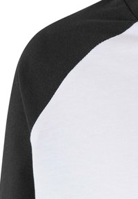 Fekete-fehér, raglán ujjú póló, sima pamut textúrával, amely a vállnál jellegzetes átlós színátmenetet mutat.