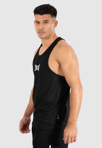 Schwarzes Tanktop mit gerippter Textur, breiten Trägern und einem kleinen weißen Logo auf der Vorderseite. Entworfen für Sportbekleidung, taillierte Silhouette.