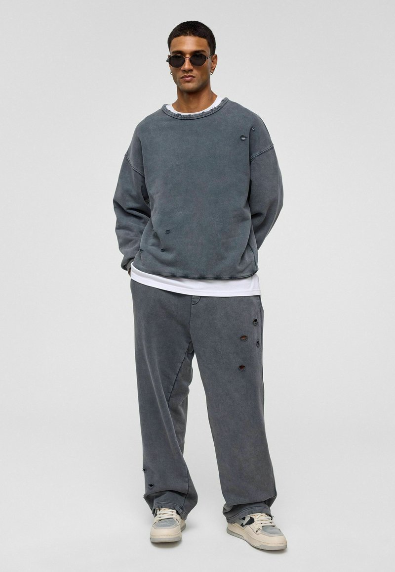 Grijze katoenen oversized sweatshirt met verwaarloosde accenten, gecombineerd met bijpassende losse broek met vergelijkbare scheuren en details.