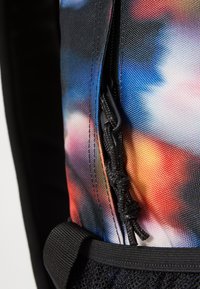 Multi-colored fabric backpack featuring a vibrant pattern, a zipper with a pull cord, and a textured black mesh accent at the bottom.