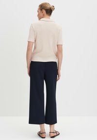 Hellrosa geripptes Polohemd mit kurzen Ärmeln, kombiniert mit dunkelblauen, weit geschnittenen Hosen und schwarzen flachen Sandalen, von hinten betrachtet.