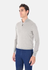 Maglione grigio chiaro a maniche lunghe con zip quarti in morbido tessuto a maglia, con orlo e polsini a coste, abbinato a pantaloni blu scuro.