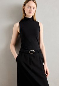 Black sleeveless top with a high neckline, paired with a black belt featuring a gold buckle, set against a neutral background.
