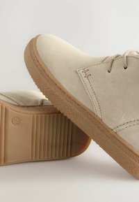 Chaussures en daim beige avec un bout rond, un design à lacets et une semelle en caoutchouc texturée. Présentent une semelle en caoutchouc beige avec des accents striés.