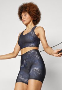 Svart sport-BH og høyt midjeshorts med blå geometriske mønstre. Laget av elastisk materiale, med en tettsittende design og flate sømmer.