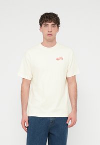 Κρεμ κοντομάνικη μπλούζα από βαμβά κι, με μικρό κόκκινο σχέδιο skateboard στο αριστερό μέρος του στήθους. Casual εφαρμογή με στρογγυλή λαιμόκοψη.