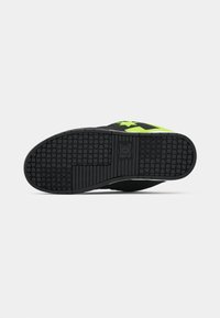 Schwarze Skateboardschuhe mit einer Gummisohle, die über einen strukturierten Grip verfügt, und einem leuchtend grünen Stern-Design an der Seite.