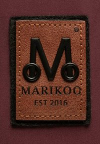 Brown leather label featuring black embossed logo “M” with circular accents, and text "MARIKOO EST 2016," bordered with black felt and orange stitching.