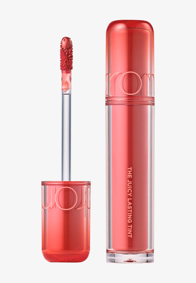 Tube de teinte pour les lèvres couleur corail rose avec applicateur assorti, étiqueté "THE JUICY LASTING TINT", sur un fond blanc.