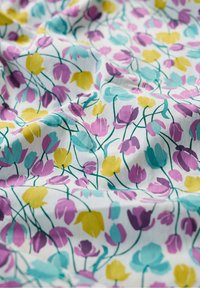 Tela blanca con un patrón floral presenta formas de tulipanes en púrpura, turquesa y amarillo sobre una superficie texturizada, creando un diseño vibrante.