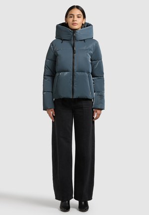 Steppjacke in gedämpftem Türkis mit hohem Kragen, Reißverschluss und Seitentaschen. Glatte, glänzende Oberfläche mit einer leicht voluminösen Silhouette.