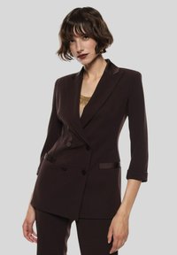 Blazer marrone doppiopetto con revers in satin, maniche a tre quarti e dettagli in bottone. Texture liscia, vestibilità su misura.