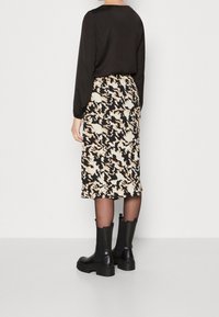 Camisa negra de manga larga combinada con una falda estampada en crema y negro. El conjunto se complementa con botas negras de tobillo grueso.