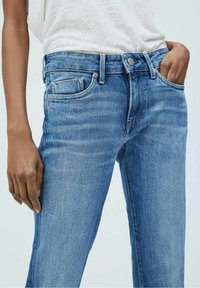 Jeans de mezclilla de color azul claro con una cintura de altura media, cinco bolsillos y una textura suave. Presentan un desvanecimiento sutil y un corte recto clásico.