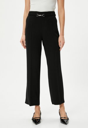 Black wide-leg trousers with a tailored design, featuring a silver buckle belt and smooth, textured fabric. Shiny pointed-toe heels.