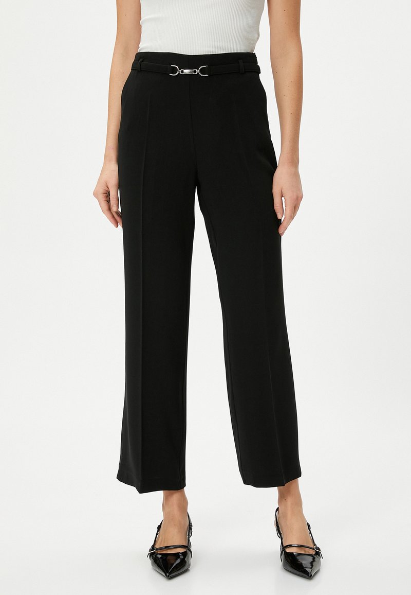 Zwarte wijde broek met een op maat gemaakte uitstraling, voorzien van een zilveren gespsriem en een gladde, gestructureerde stof. Glanzende puntige hakken.