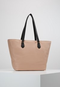 Beżowa torba typu tote z faux skóry z czarnymi, teksturowanymi uchwytami i eleganckim designem. Posiada przestronną kieszeń wewnętrzną oraz delikatne detale przeszycia.