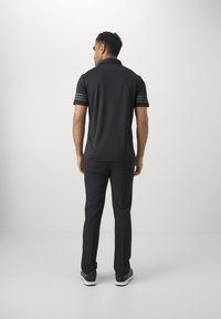 Black polo shirt with short sleeves, featuring three horizontal stripes on the sleeves, paired with black trousers and dark athletic shoes.