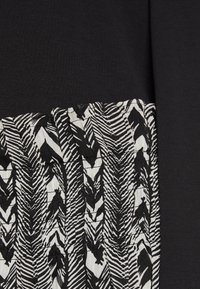 Tissu noir avec un design texturé présentant un motif de feuilles blanches et noires. Les deux sections contrastantes se rejoignent avec des bords froncés.