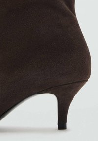 Chaussure à talon en daim marron avec un design effilé, dotée d'un talon aiguille noir bas et d'une finition lisse. Aucun motif ni quincaillerie visibles.