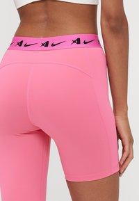 Roze atletske kratke hlače s crnim logom na struku, koje imaju glatki, prilagođeni dizajn i detalje šavova za udobnost.