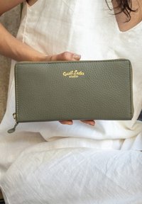 Oliven grøn læderpung med en tekstureret overflade og et gylden logo, der har en lynlås lukning og en lille dekorativ trækkrog.