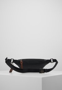 Černá kožená ledvinka se zipem, nastavitelným popruhem a hnědým akcentem. Úzký, aerodynamický tvar se hladkým povrchem.