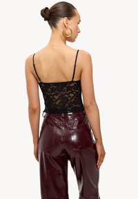 Zwarte kanten top met verstelbare bandjes, gedragen met glanzende burgundy patenten leren broek met achterzakken en een zachte textuur.