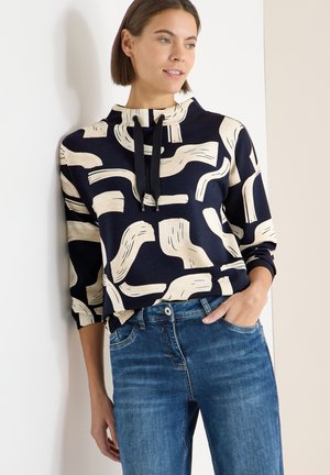 Sweat à capuche bleu marine avec un motif abstrait beige, doté d'une capuche à cordon, de manches longues, et assorti à un jean bleu clair.