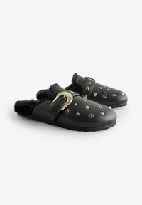 Svarta lädersandaler med tjockt fuskpälsfoder, prydda med gyllene stjärnor och prickar, samt en bred rem med dekorativt beslag.