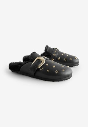 Svarta lädersandaler med tjockt fuskpälsfoder, prydda med gyllene stjärnor och prickar, samt en bred rem med dekorativt beslag.