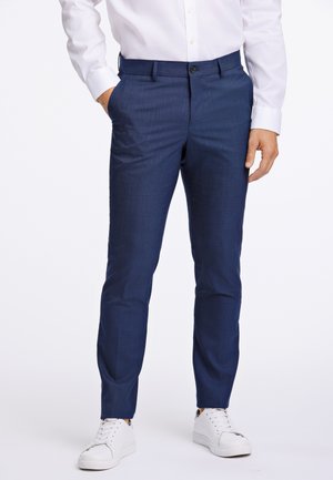 Navyblauwe op maat gemaakte broek met een subtiele textuur, voorzien van zijzakken en een knoopsluiting, gecombineerd met witte sneaker.
