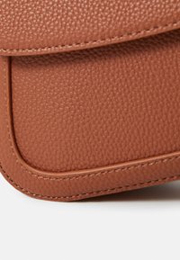 Coin d'un sac en cuir texturé marron, avec un bord lisse orné de coutures contrastées et un motif de grain subtil.