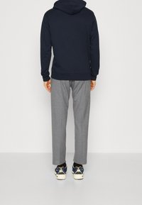 Sudadera azul marino con capucha ajustable, pantalones de cuadros grises y zapatillas multicolor, con acentos contrastantes.