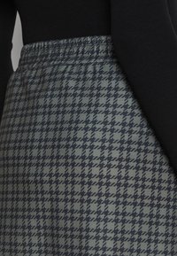Houndstooth-mönstrad kjol i dämpad grön och marinblå, med elastisk midja och en slät textur. Närbild.