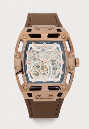 Montre avec bracelet en caoutchouc marron, boîtier rectangulaire de couleur bronze, cadran transparent révélant les mécanismes internes, accents roses et grands marqueurs horaires.