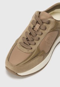 Botte brune en daim et matériaux synthétiques. Présente un bout rond, une languette rembourrée, des lacets texturés et des accents de logo sur le côté.