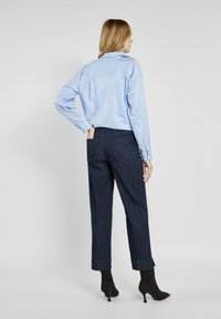 Jasnoniebieska koszula z długim rękawem i kołnierzykiem w kształcie szpilki, połączona z ciemnoniebieskimi spodniami dżinsowymi z podwiniętym dołem i tylnymi kieszeniami.