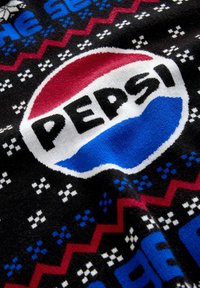 Gestrickter Stoff mit einem roten, weißen und blauen Pepsi-Logo, umgeben von geometrischen Mustern in Schwarz, Weiß, Rot und Blau.