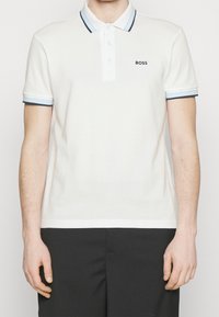 Bílé polo tričko vyrobené z bavlny, s dvoubarevným zapínáním na knoflíky, kontrastním modrým a černým žebrovaným límcem a manžetami, s logem "BOSS".
